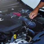 Auto mechanic inspecting a car engine while using a tablet during a fall vehicle tune-up and maintenance check.